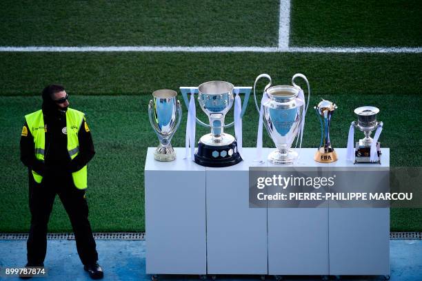 Security staff member stands guard next to the trophies of the UEFA Super Cup, the Spanish League, the UEFA Champions League, the FIFA Club World Cup...