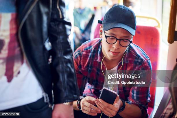 young man on city tram looking at smartphone and listening to earphones - mens en machine stockfoto's en -beelden