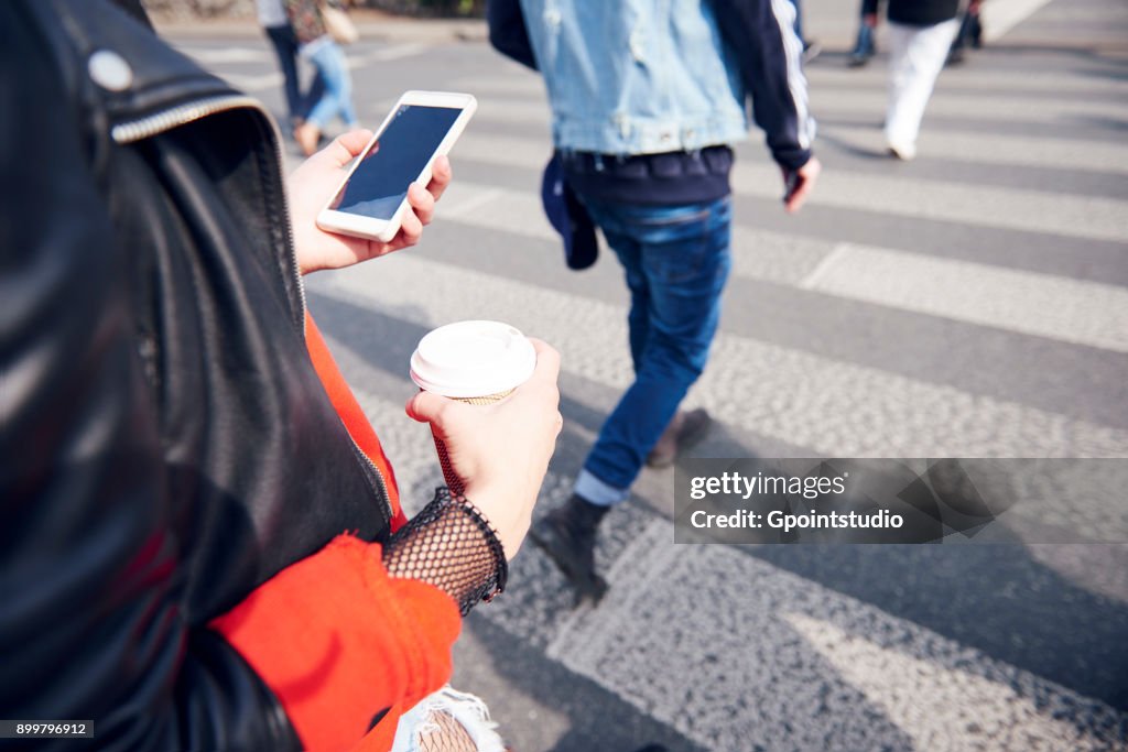 Person on pedestrian crossing with coffee and smartphone