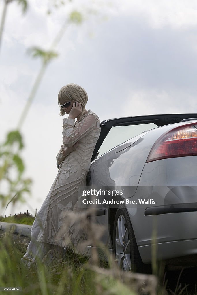 Woman leaning on a car at the roadside on a mobile