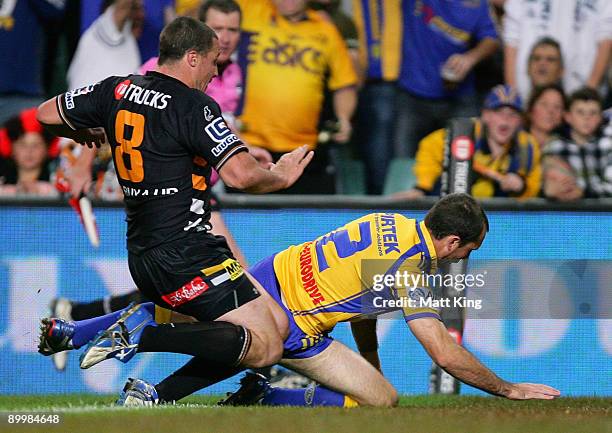 Luke Burt of the Eels is kneed in the back by Bryce Gibbs of the Tigers as he scores a try during the round 24 NRL match between the Wests Tigers and...