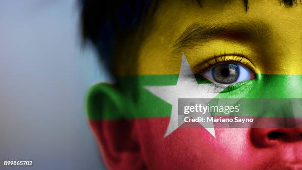 boy's face, looking at camera, cropped view with digitally placed burma flag on his face. - myanmar war stock pictures, royalty-free photos & images