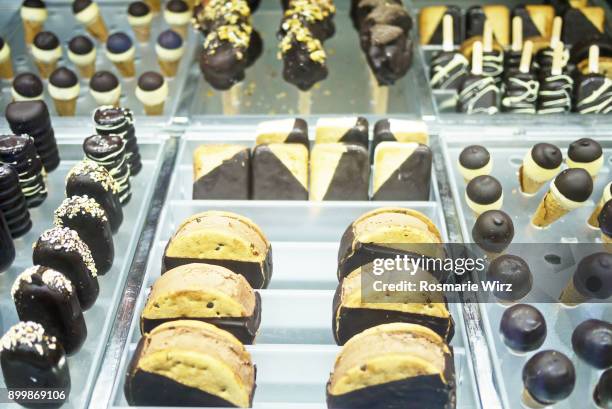 chocolate pastry and ices on stick, for sale, under glass cover - close up of chocolates for sale fotografías e imágenes de stock