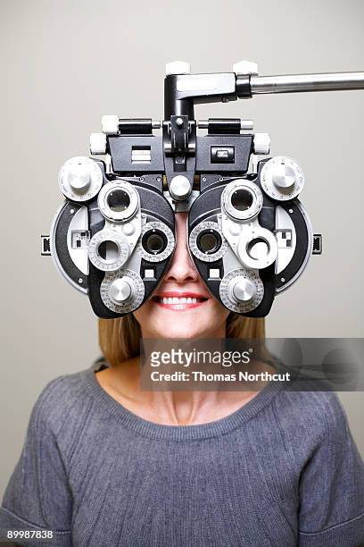 mature woman looking through phoroptor - eye test stock pictures, royalty-free photos & images