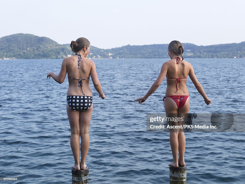 Two girls stand on posts, ready to jump into lake