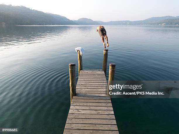 man dives from wooden pier into calm lake water - lake orta stock pictures, royalty-free photos & images