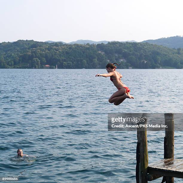 girl jumps into lake while friend looks on - lake orta stock pictures, royalty-free photos & images