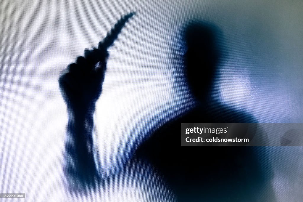 Violent threatening silhouette of man wielding a knife behind frosted glass window