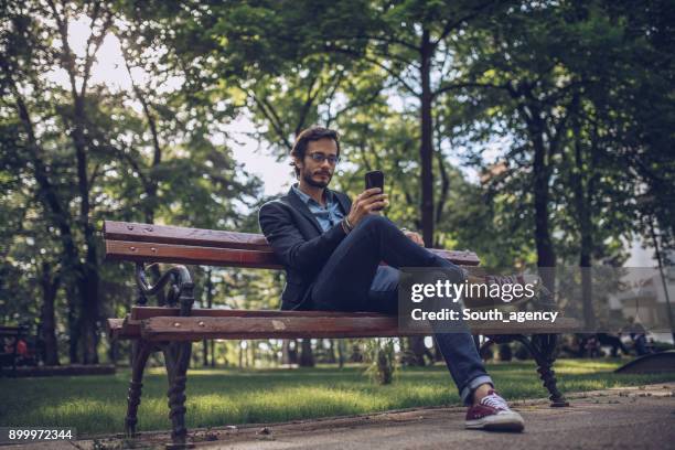 businessman texting in public park - public park bench stock pictures, royalty-free photos & images