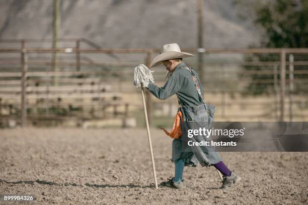 a young boy, acting as a rodeo clown, holds a mop used as his horse. - rodeo clown stock pictures, royalty-free photos & images