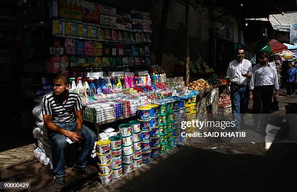 Palestinians walk past a shop as a vendor waits for customers at a popular market in Rafah in the southern Gaza Strip on the first day of the Muslim...