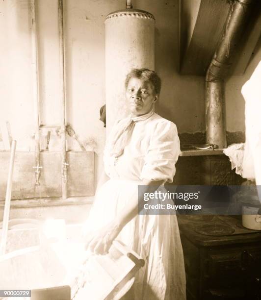 African American, standing by a washtub with her hand on a washboard.