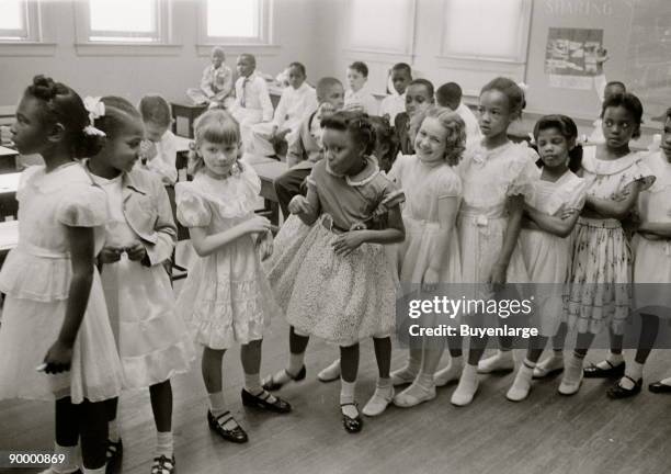 African American and white school girls standing in a classroom while boys sit behind them.