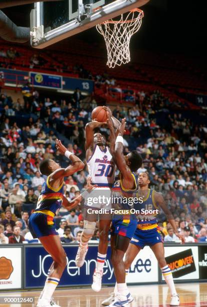 Bernard King of the Washington Bullets shoots over Alex English and T.R. Dunn of the Denver Nuggets during an NBA basketball game circa 1988 at the...