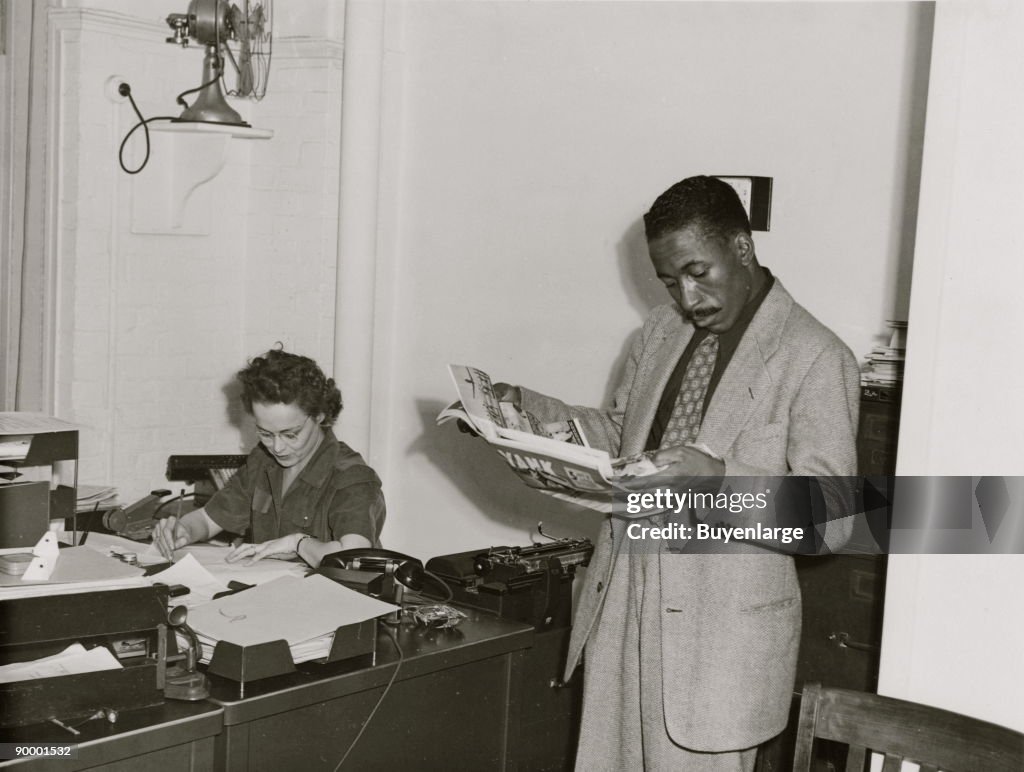 Gordon Parks, Farm Security Administration/Office of War Information photographer, standing in office with Helen Wool seated at desk