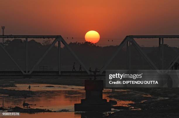 Indian people cross a railway bridge as the sun sets on the horizon for the last time this year in Siliguri on December 31, 2017. / AFP PHOTO /...