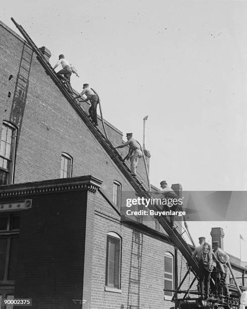 Team of Firefighters with Hoses on Their backs climbs a ladder at a firefighter's school