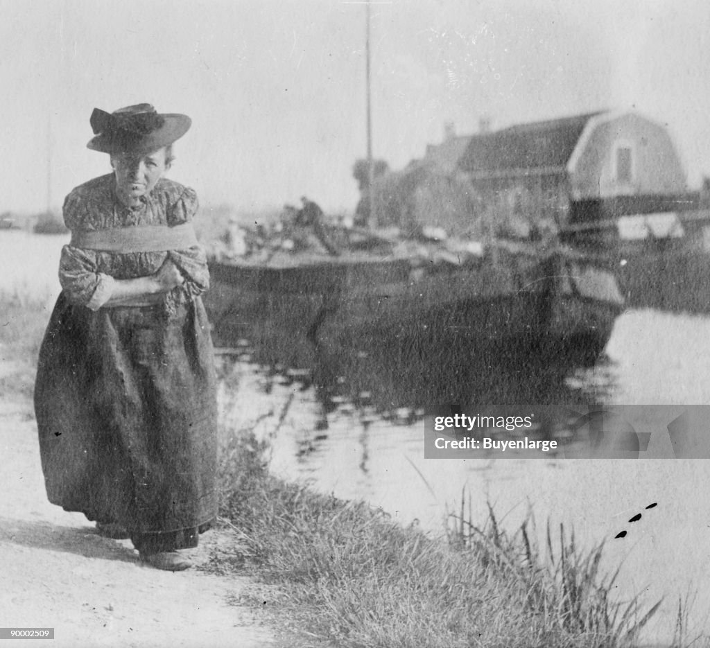 A Older Dutch woman has a bustle around her chest as she pulls a barge down a canal.