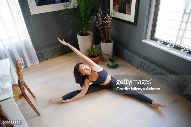 fit asian woman stretching in a yoga pose in an apartment setting - legs apart stock pictures, royalty-free photos & images