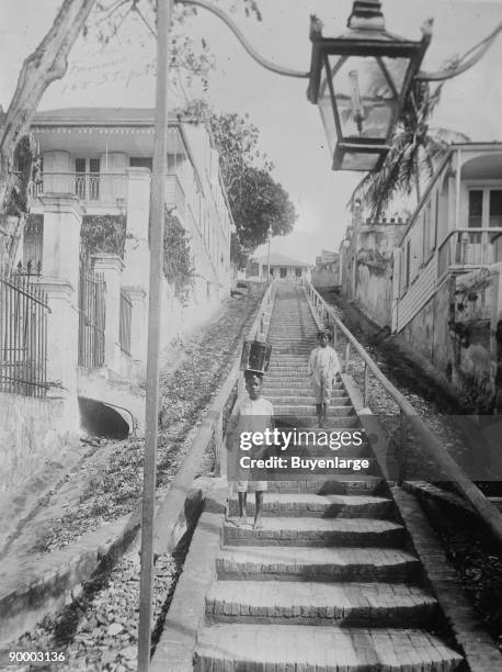 St. Thomas -- Charlotte Amalie; a West Indian Boy Carries a Container on his head as he and another child walk down a long flight of exterior...