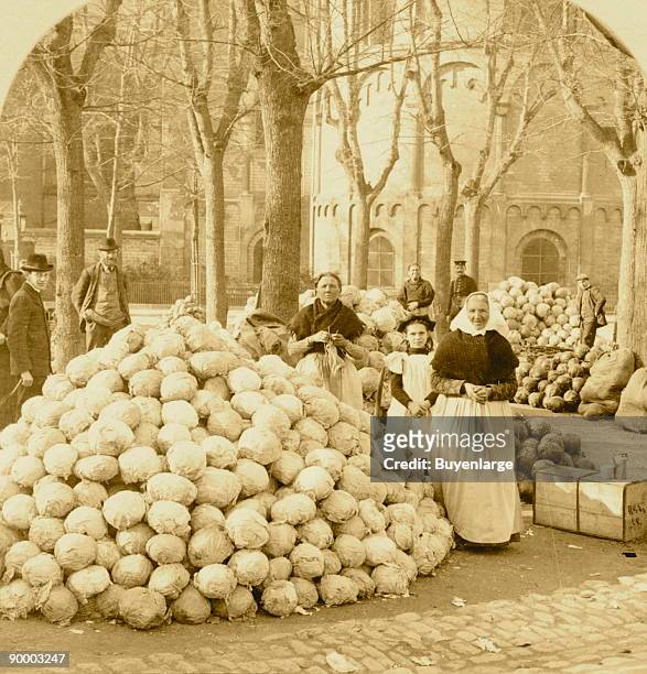 Mounds of cabbages sit by the street, as townspeople look on.