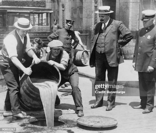 New York City Deputy Police Commissioner John A. Leach, right, watching agents pour liquor into sewer following a raid during the height of...