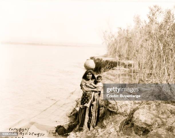 Mojave woman carrying water on her head and holding child