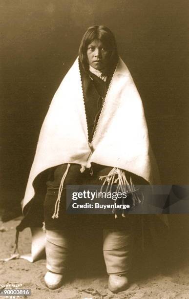 Hopi woman's bridal wear which includes thick leggings, dark dress and a white blanket draped across her shoulders.