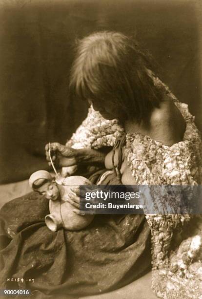 Old woman with rabbit skin blanket around shoulders, painting design on piece of pottery with yucca stem brush, Arizona.