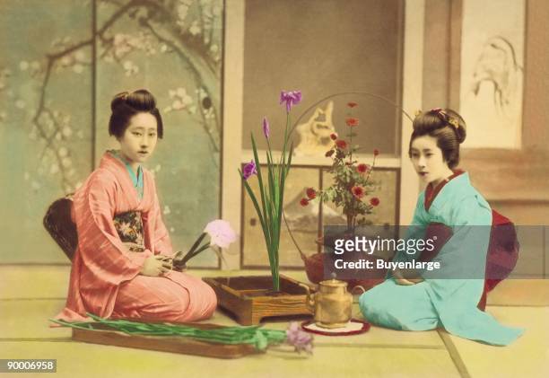 Two girls in kimono, obe and sashes arrange flowers as Ikibana in the Japanese Tradition