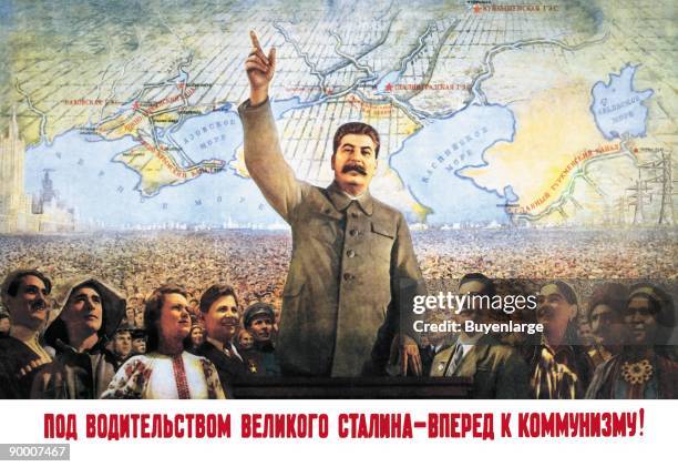 In front of a map of the world, Stalin stands with arms raised leading the masses of his people