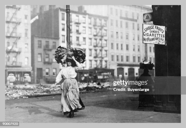 Immigrant Woman Walks Down Street Carrying a Pile of Clothing on Her Head