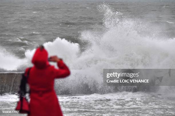 Woman takes a picture of waves breaking on the shore, on December 31, 2017 in Batz-sur-Mer, western France, a day before storm Carmen is to hit the...