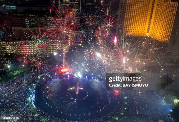 Fireworks explode over the Selamat Datang Monument in downtown Jakarta on January 1, 2018 during New Year celebrations. / AFP PHOTO / BAY ISMOYO