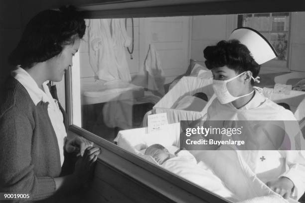 Woman looking through window at baby being held by nurse in maternity ward. Ansel Easton Adams was an American photographer, best known for his...