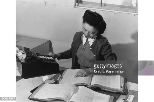 Mrs. Teruko Kiyomura, bookkeeper, seated at a desk, operating an adding machine while reading a ledger. Ansel Easton Adams was an American...