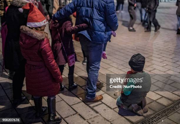 Girl wearing a Santa Claus hat stands in front of a Syrian child begging in Taksim Square in the 2018 New Year celebrations