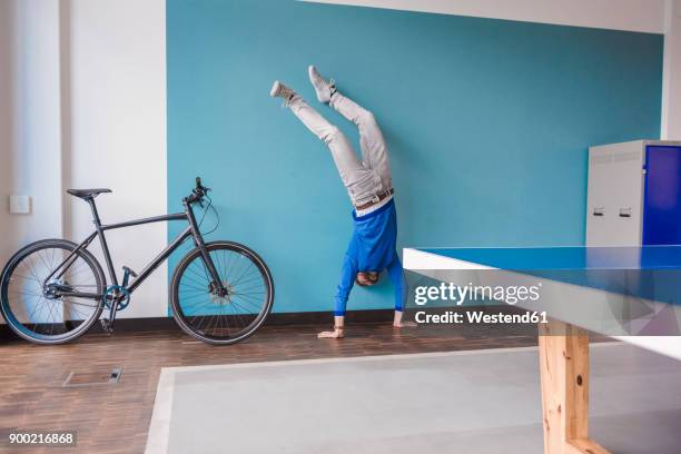 man doing a handstand in break room of modern office - fare la verticale sulle mani foto e immagini stock