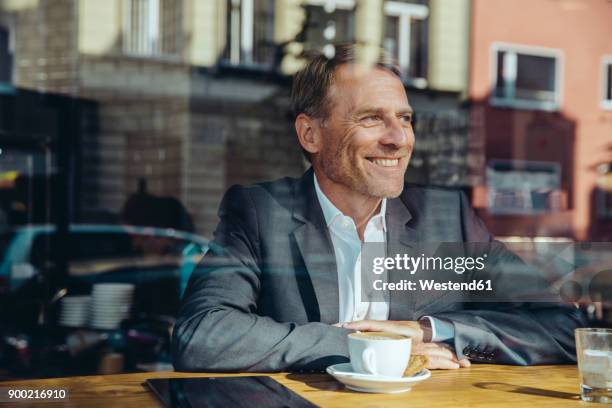 smiling businessman in cafe looking out of window - business men urban city stock-fotos und bilder