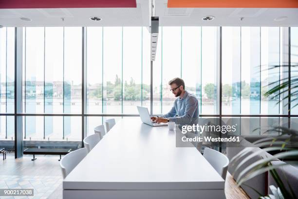 man using laptop sitting at conference table in office - conference table top stock pictures, royalty-free photos & images