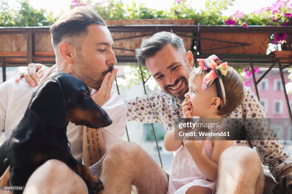 Happy gay couple with daughter and dog on balcony