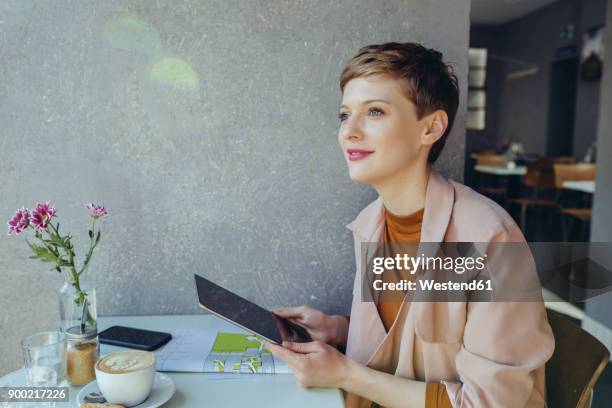 woman with a tablet in a cafe looking sideways - gründer stock-fotos und bilder