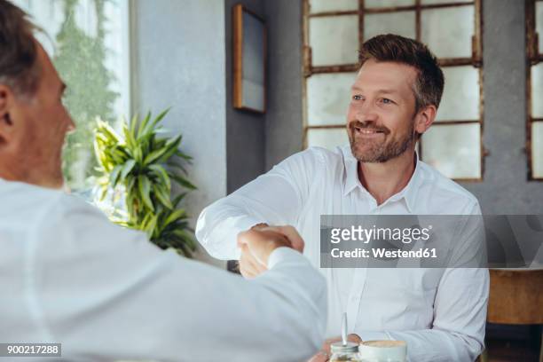 two businessmen shaking hands in cafe - abmachung stock-fotos und bilder