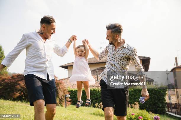 happy gay couple playing with their child in the garden - young gay couple stock pictures, royalty-free photos & images