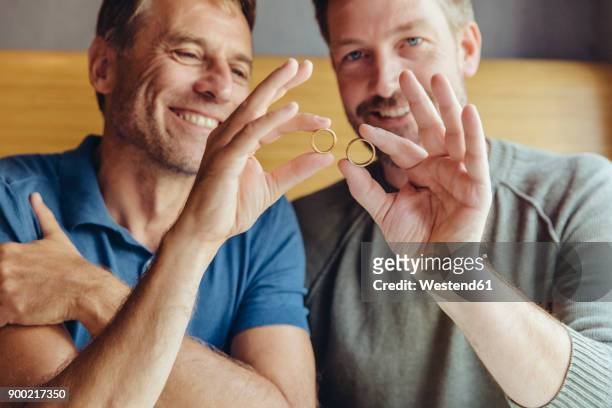 happy gay couple holding up their wedding rings - men rings foto e immagini stock