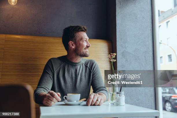 smiling mature man sitting in cafe looking out of window - tisch betrachten stock-fotos und bilder