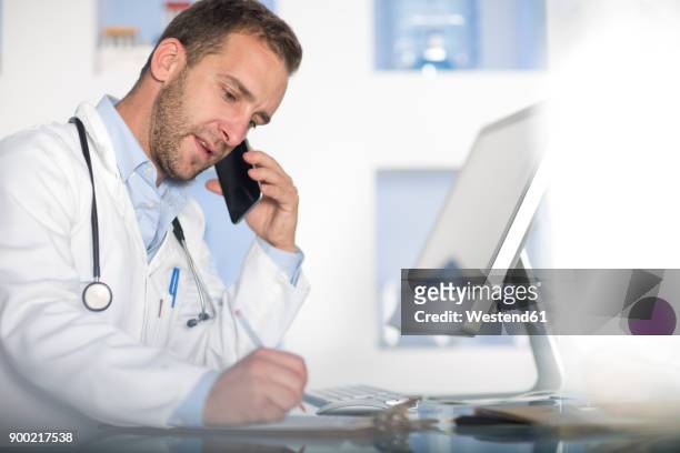 doctor at desk talking on cell phone - doctor phone stock pictures, royalty-free photos & images
