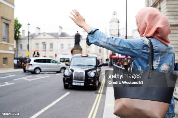 uk, england, london, young woman wearing hijab hailing a taxi - hijab woman from behind stock-fotos und bilder