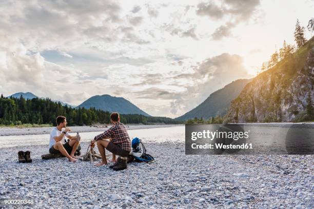 germany, bavaria, two hikers having a rest on gravel bank in the evening - inocente fotografías e imágenes de stock