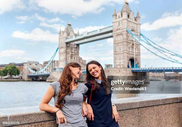 uk, london, two smiling women near the tower bridge - london landmark stock-fotos und bilder